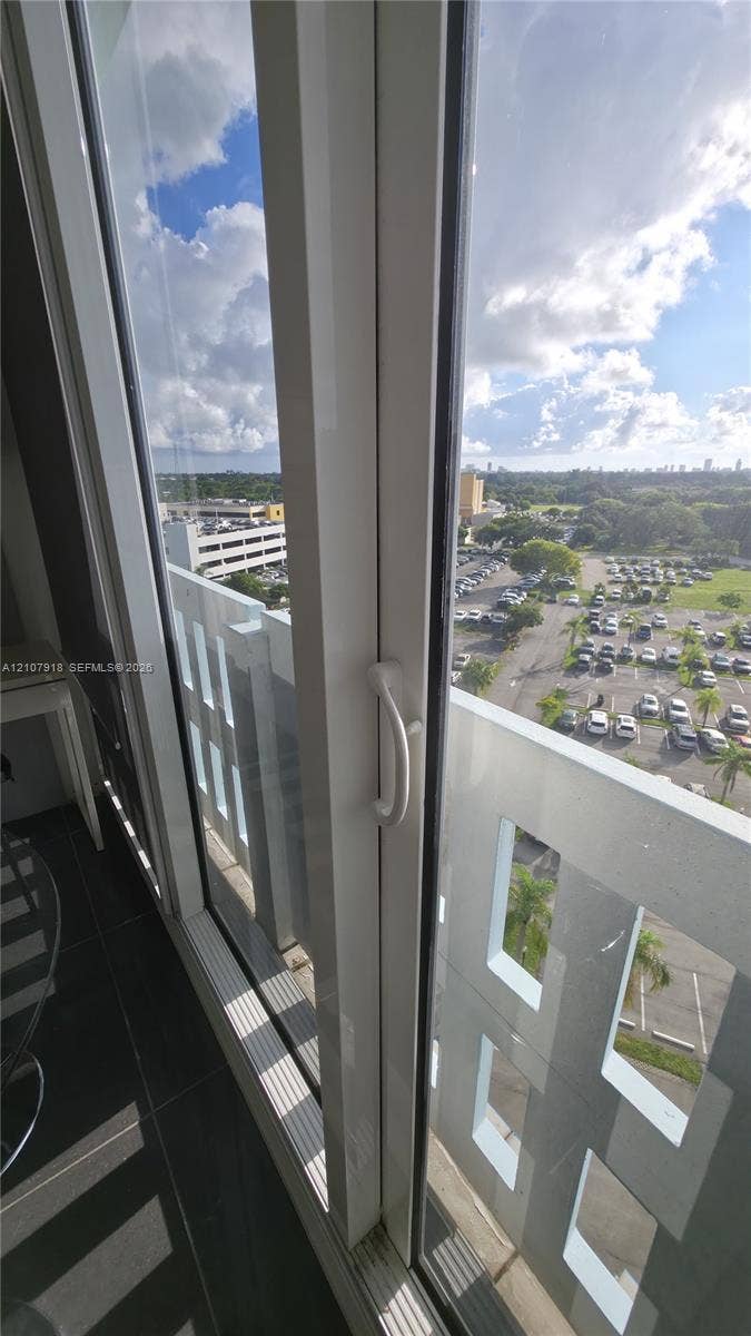 Floor-to-ceiling glass door with white frame and vertical handle, opening to a private balcony with decorative concrete railing