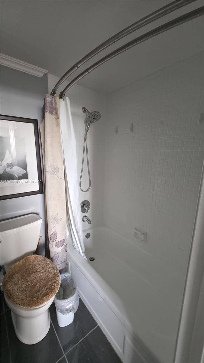 Tub-shower combination featuring white subway tile surround, curved metal shower rod, handheld shower fixture, and dark tile flooring