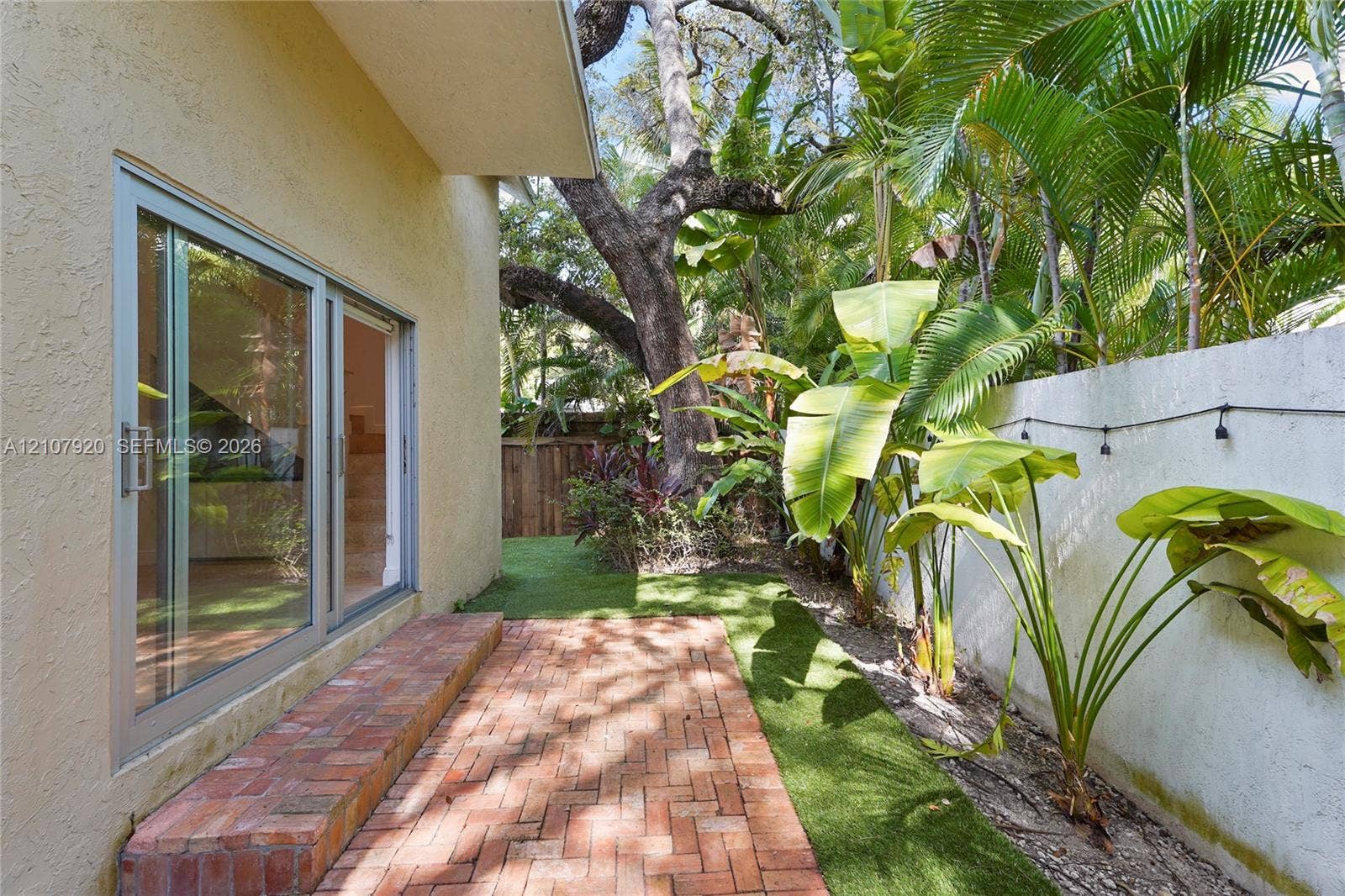 3062 Shipping Avenue, #3062, Miami, Miami, FL 33133 Exterior patio featuring red brick paving, sliding glass doors, synthetic turf landscaping, and a concrete masonry wall