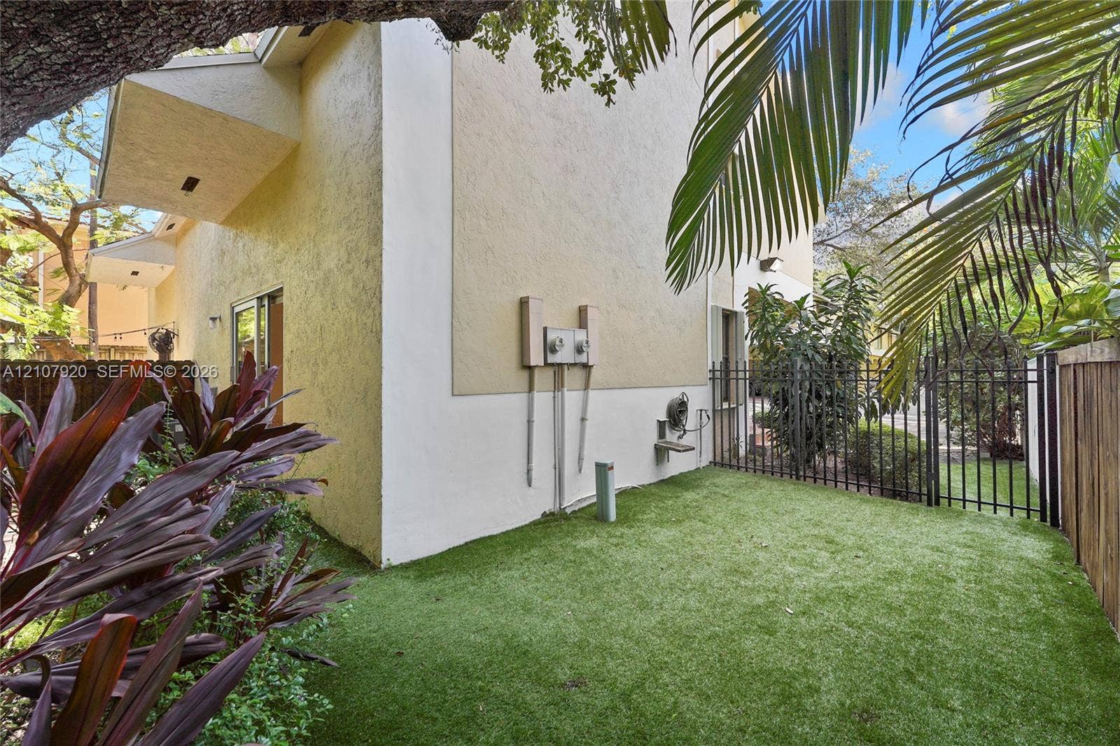 3062 Shipping Avenue, #3062, Miami, Miami, FL 33133 Stucco exterior, fenced yard with synthetic turf, mature landscaping, and sliding glass door entry