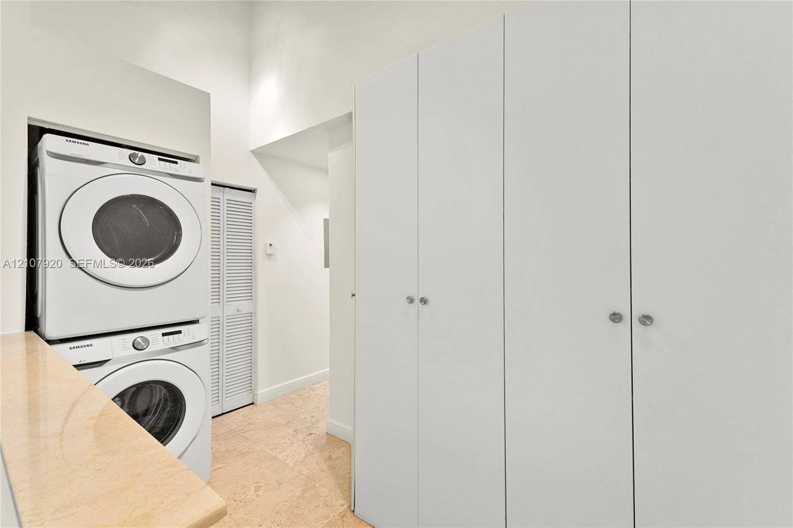 3062 Shipping Avenue, #3062, Miami, Miami, FL 33133 Laundry area featuring floor-to-ceiling built-in cabinetry, stacked appliances, stone-surface countertop, and louvered closet doors