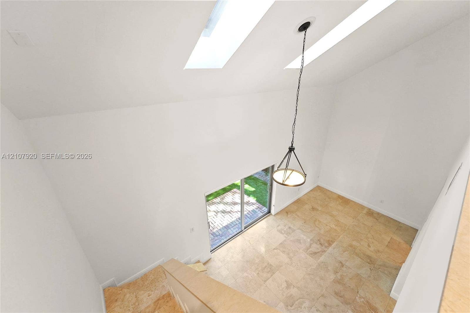 3062 Shipping Avenue, #3062, Miami, Miami, FL 33133 Vaulted ceiling featuring dual skylights, stone tile flooring, and a suspended chandelier, with sliding glass doors opening to a paved exterior space