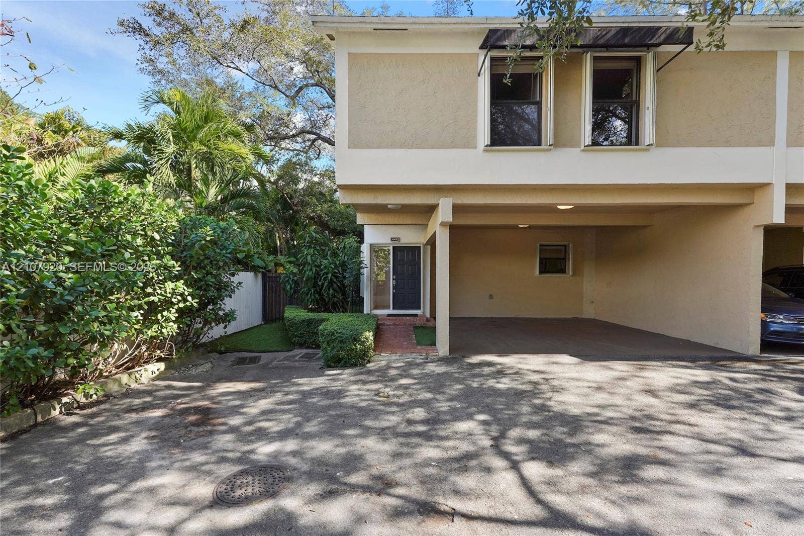 3062 Shipping Avenue, #3062, Miami, Miami, FL 33133 Two-story exterior featuring a covered carport, brick paver entryway, dark-frame windows with metal awnings, and landscaped surroundings