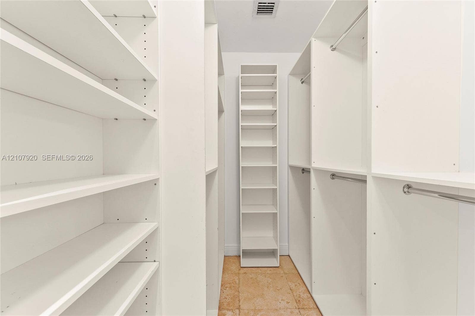 3062 Shipping Avenue, #3062, Miami, Miami, FL 33133 Walk-in closet featuring white custom built-in shelving, adjustable storage units, metal garment rods, and stone-tile flooring
