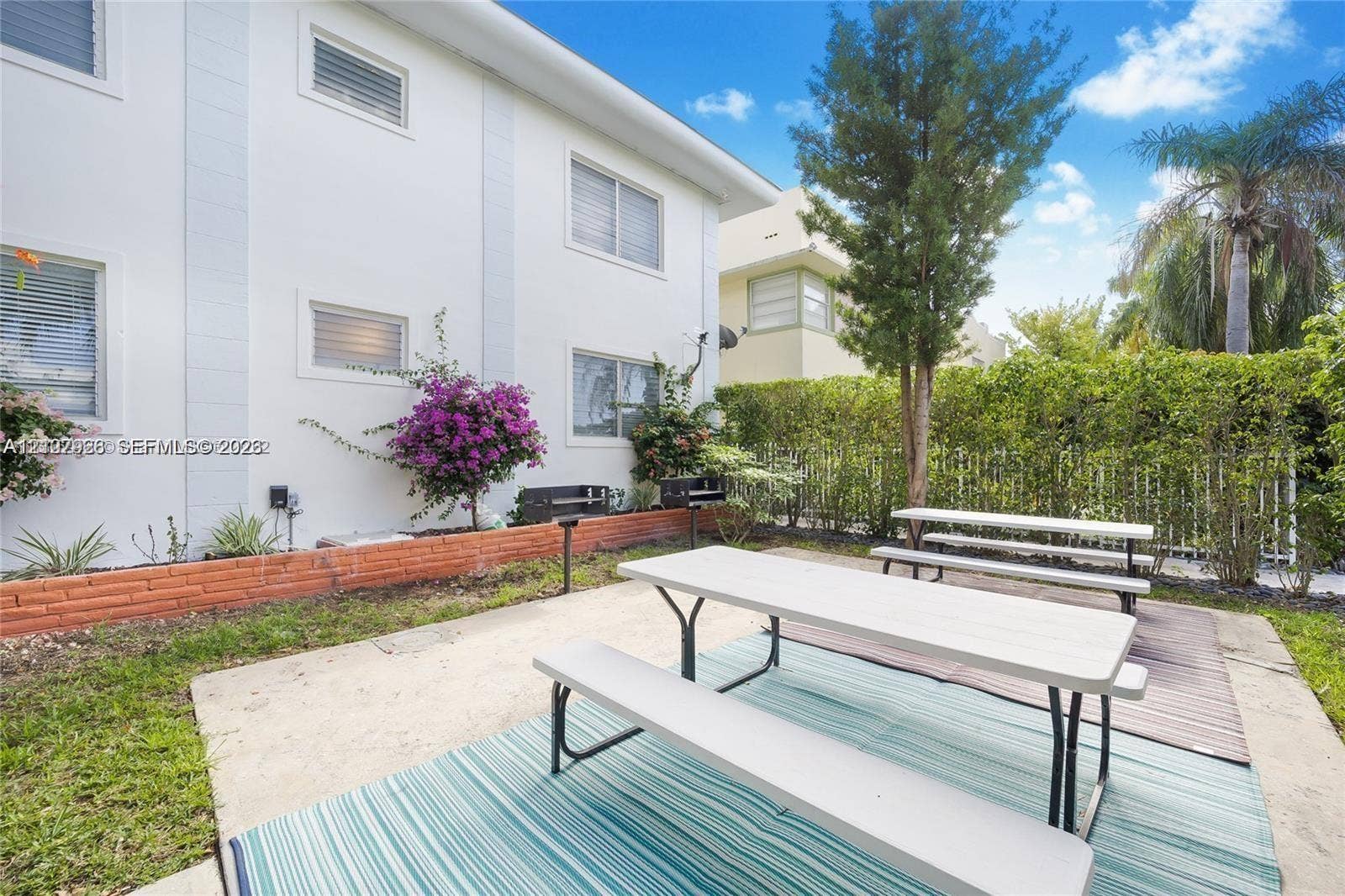 Outdoor recreation area featuring a concrete patio, built-in charcoal grills, low-profile brick retaining wall, and mature landscaping
