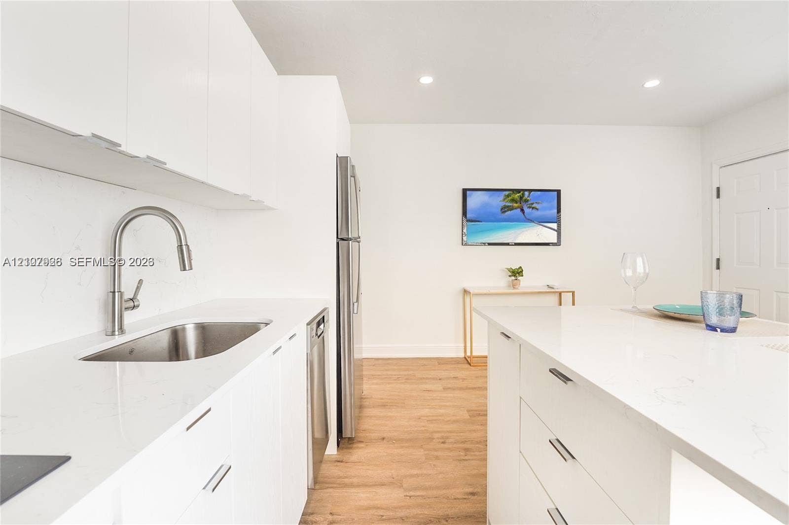 Kitchen featuring white flat-panel cabinetry, a stainless steel undermount sink with a gooseneck faucet, light-toned stone-finish countertops, stainless steel appliances, and wood-finish flooring