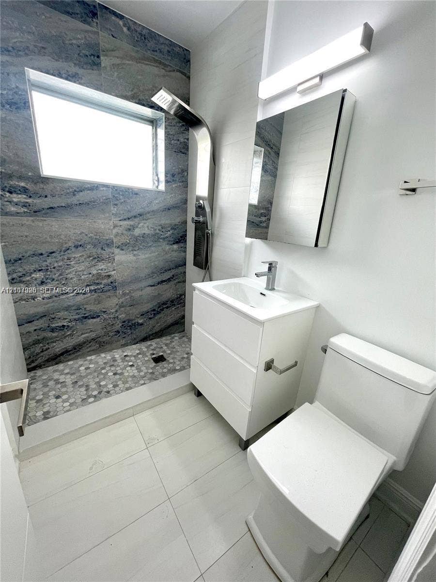 Bathroom featuring a walk-in shower with stone-look wall tiling and a pebble-tiled floor, a wall-mounted shower panel system, a white vanity with an integrated sink, and a mirrored medicine cabinet