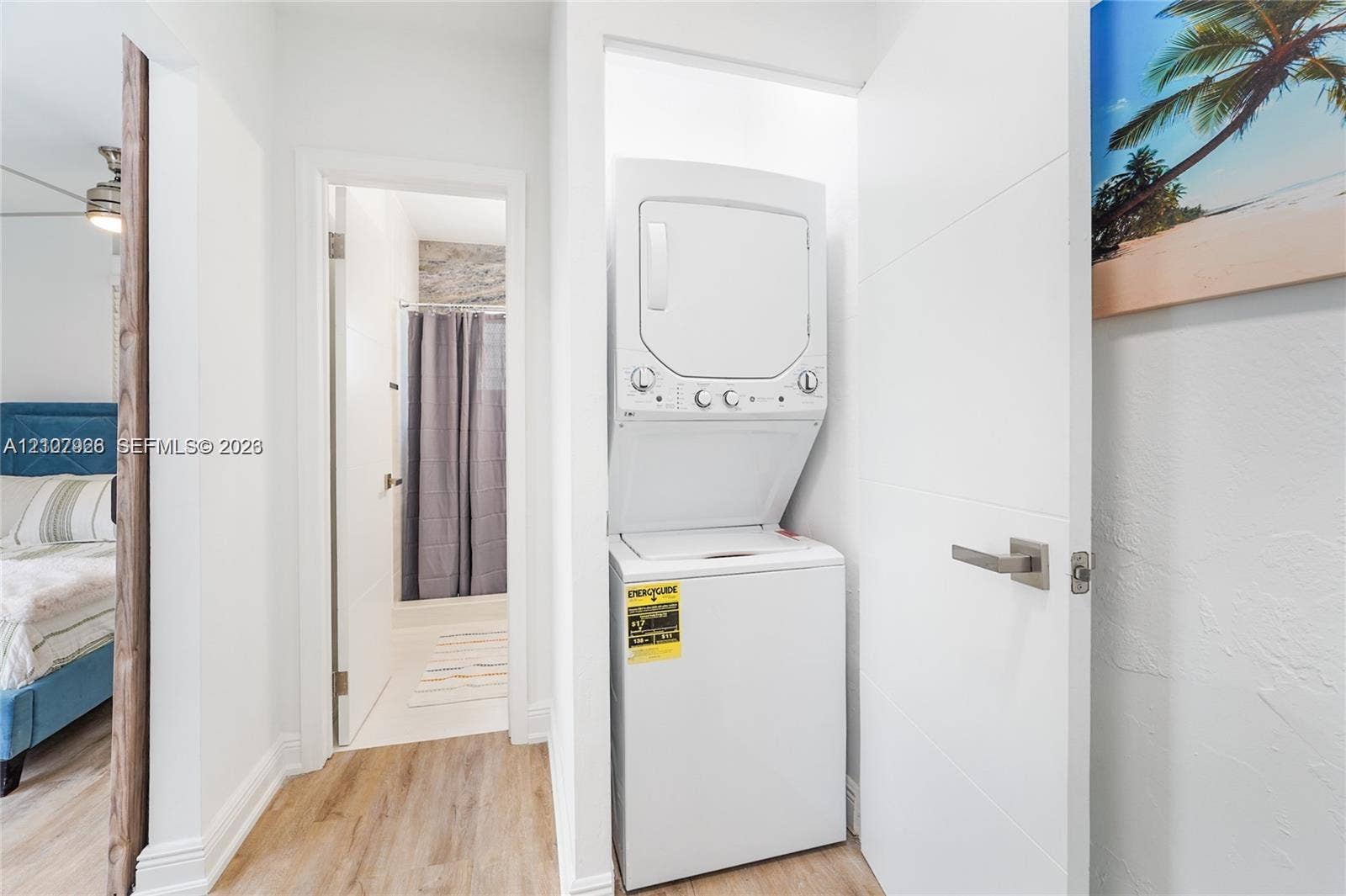 Stacked laundry unit housed within a built-in closet, featuring neutral walls, wood-finish flooring, and a sleek paneled door with satin-finish hardware