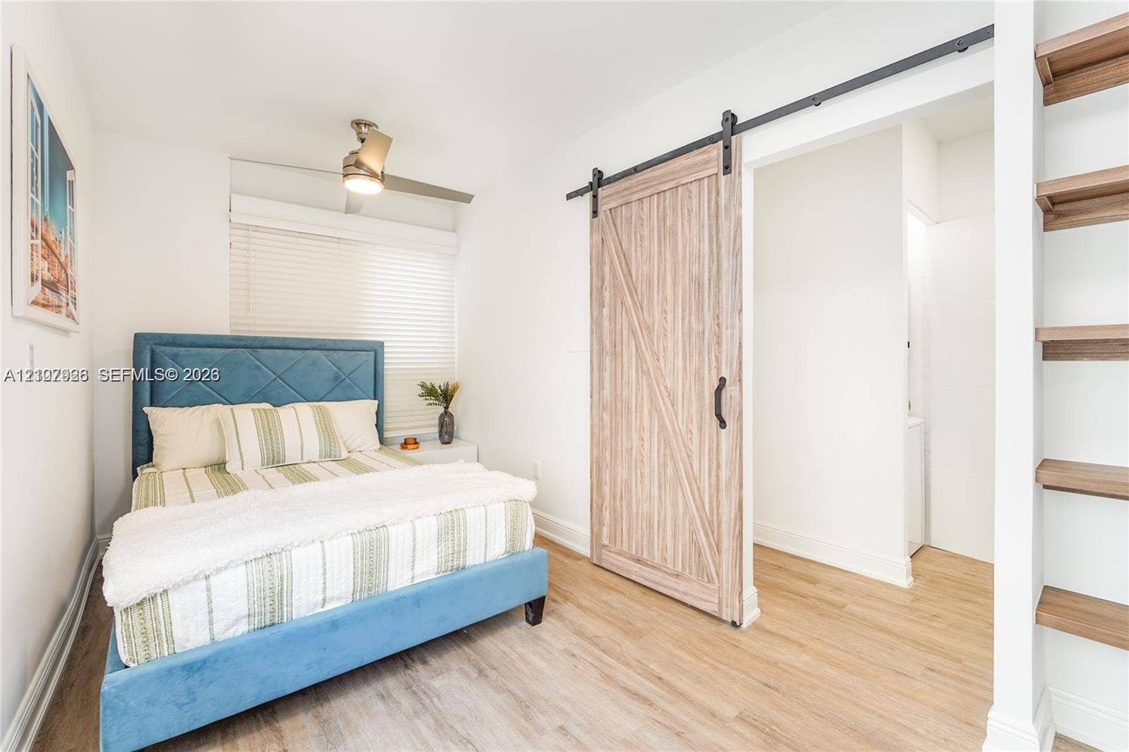 Wood-finish flooring, sliding barn door with black hardware, built-in wooden shelving, and ceiling-mounted light fixture