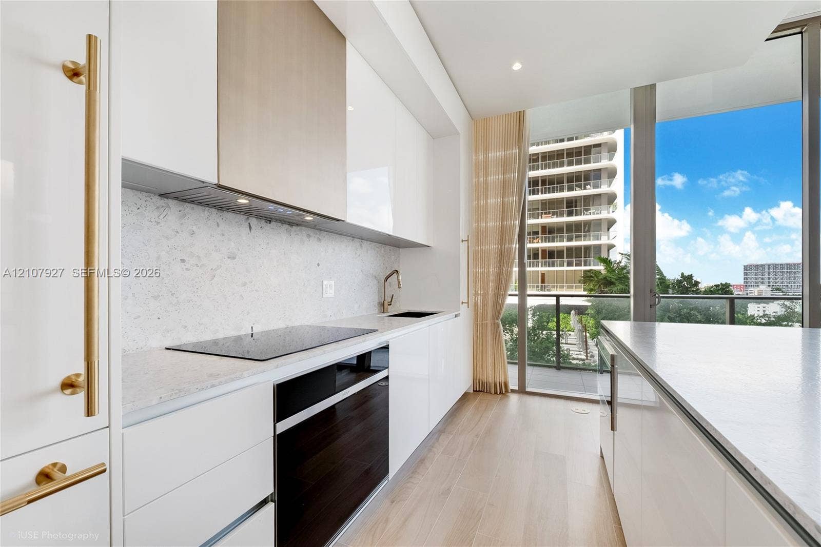 Sleek kitchen featuring high-gloss cabinetry, stone-finish countertops, an integrated cooktop, wood-finish flooring, and floor-to-ceiling glass paneling