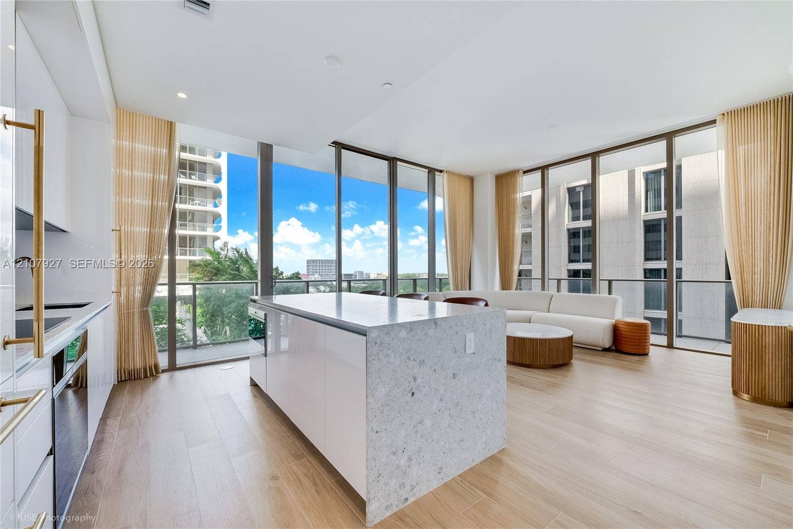 Kitchen featuring a central island with a stone-finish countertop, high-gloss cabinetry, floor-to-ceiling glass windows, and wood-finish flooring