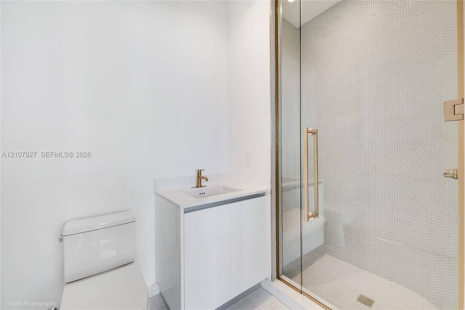 Modern bathroom featuring a glass-enclosed shower with small-format tile surround, a minimalist vanity with a white countertop and gold-tone faucet, and a sleek, low-profile toilet