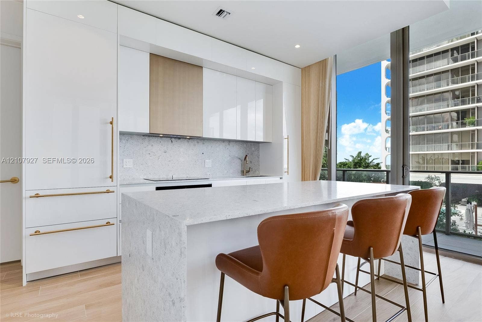 Modern kitchen featuring high-gloss cabinetry, a stone-surfaced waterfall island, integrated appliances, and wood-finish flooring