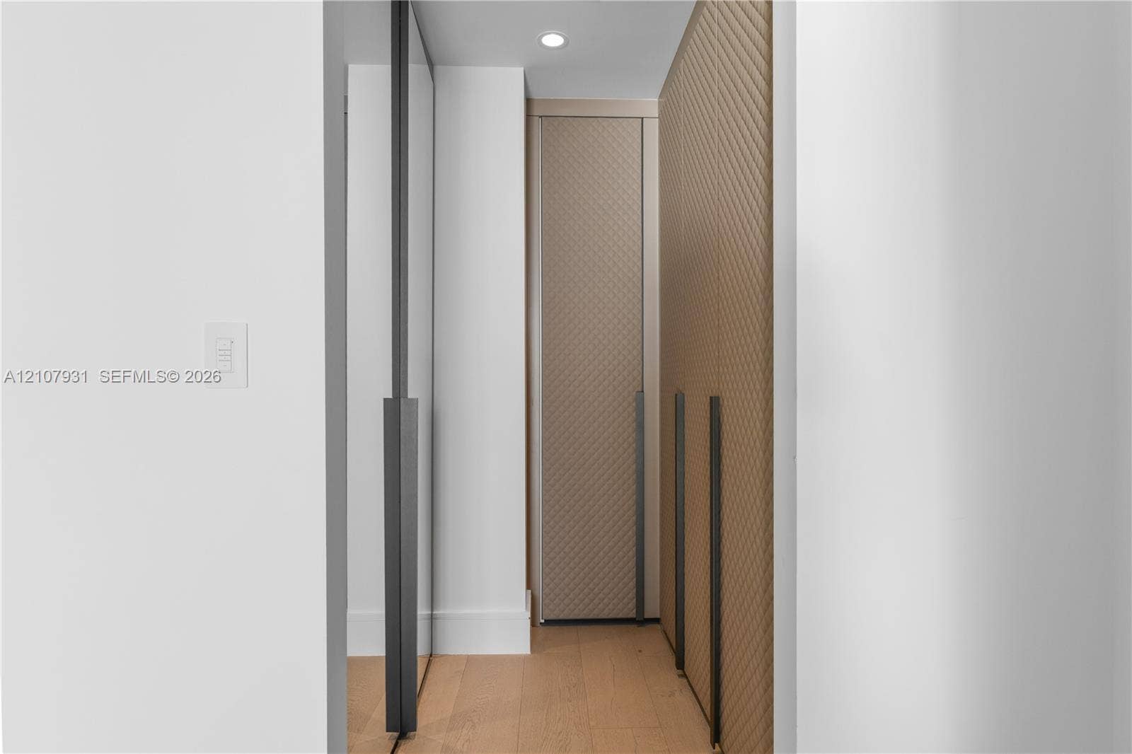 Custom built-in cabinetry with textured, diagonal-patterned detailing, full-length dark metallic hardware, integrated recessed lighting, and wood-finish flooring