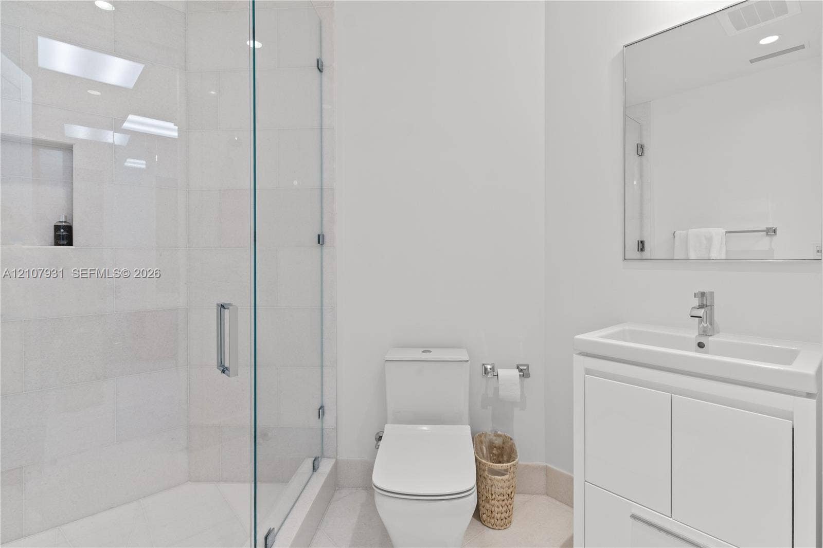 Bathroom featuring a walk-in shower with glass enclosure and tiled walls, built-in shower niche, floating-style vanity with rectangular sink, and wall-mounted mirror