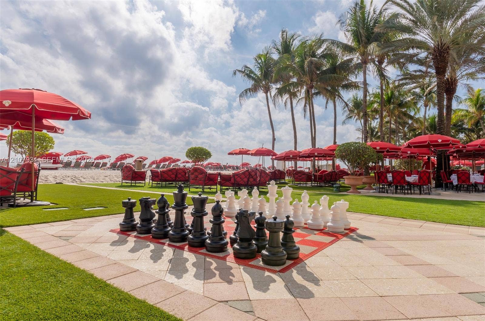 Outdoor space featuring a large-scale hardscape chessboard, manicured lawn, stone tile patio, and mature palm trees