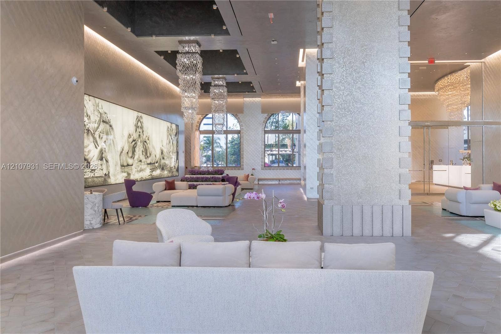 Grand lobby featuring a high-contrast coffered ceiling, tiered crystal chandeliers, stone-clad structural columns, arched windows, and large-scale backlit wall art