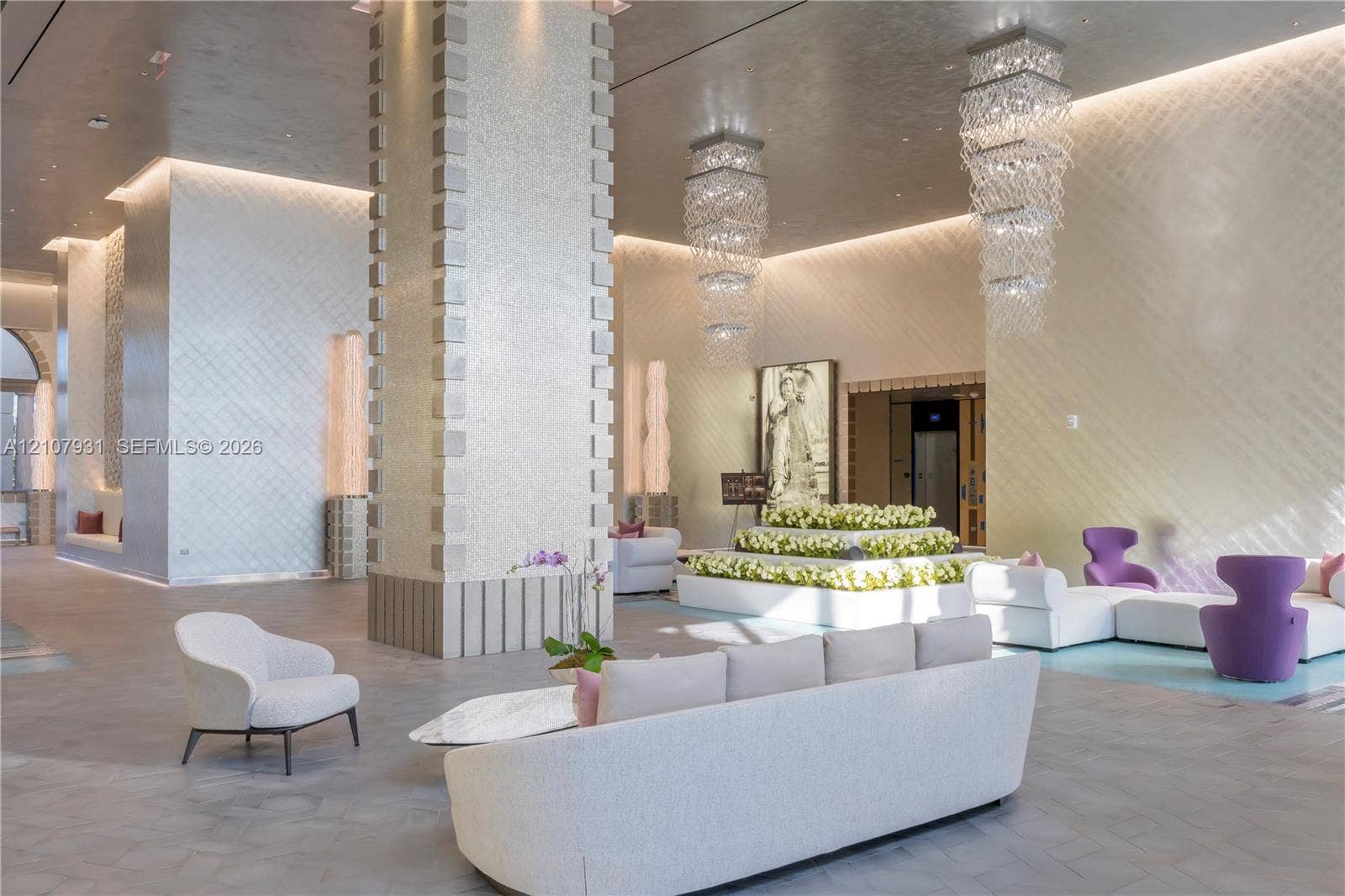 Grand lobby featuring a double-height ceiling, tiered crystal chandelier lighting, textured wall finishes, large-scale structural support pillars, and recessed cove lighting