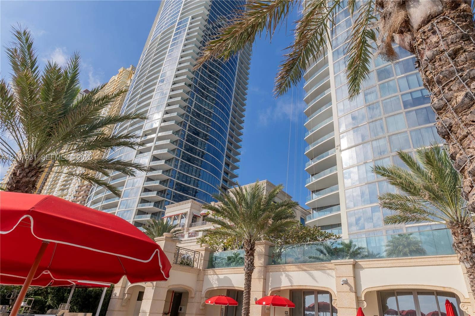 High-rise glass facade featuring wraparound balconies, decorative stone-finish exterior walls, and manicured palm trees
