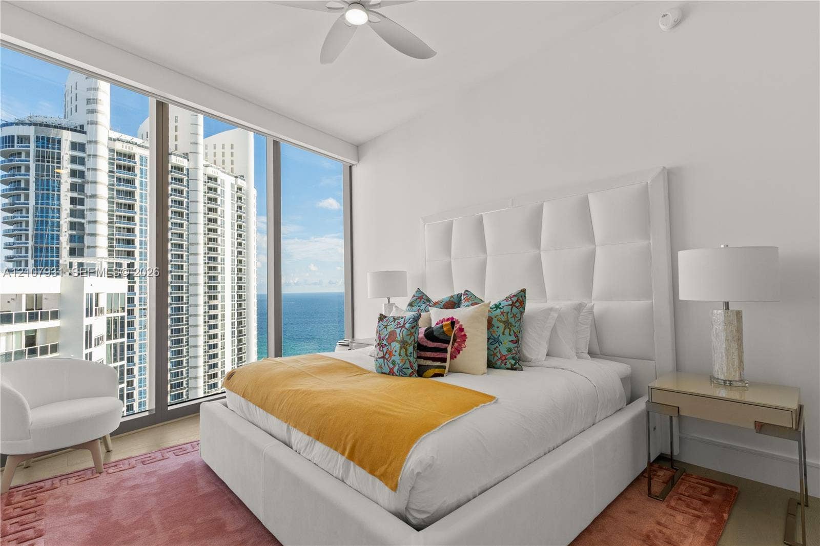 Floor-to-ceiling windows, ocean horizon backdrop, and a contemporary ceiling fan