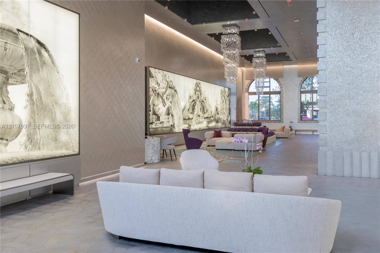 Grand foyer featuring high ceilings with recessed lighting, tiered crystal chandeliers, large-format mural wall installations, arched windows, and herringbone pattern stone-finish flooring
