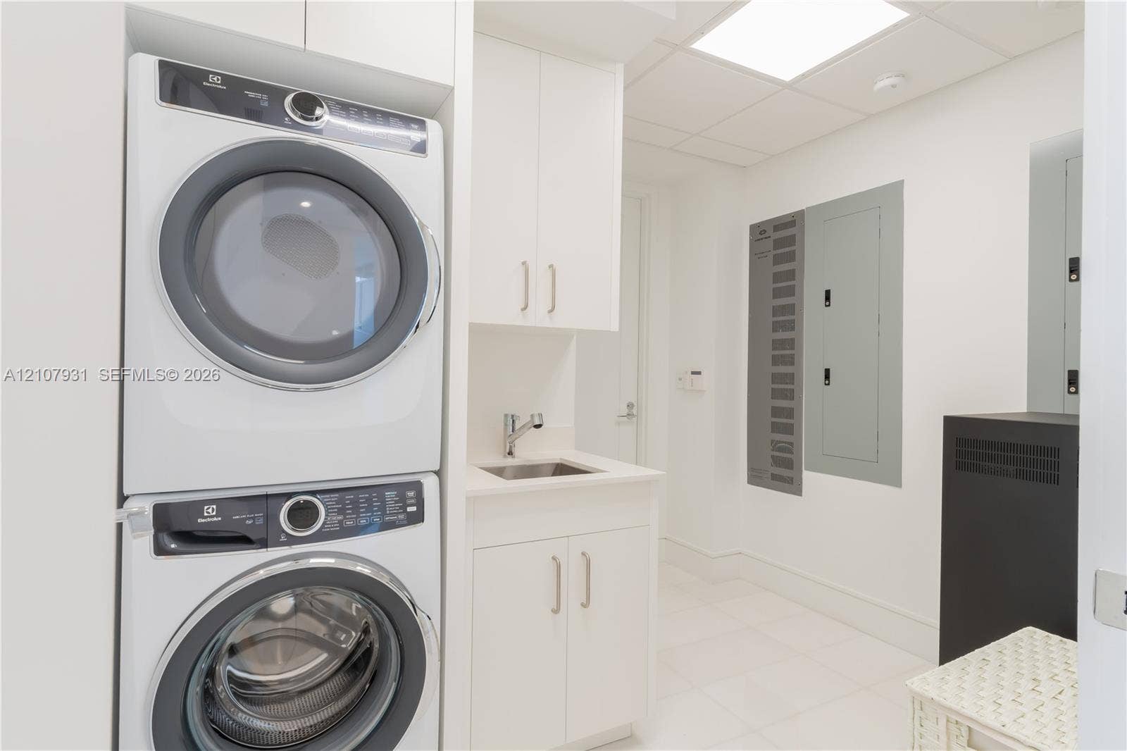 Laundry room featuring a stacked appliance set, white cabinetry, a built-in sink with a chrome faucet, and tile flooring
