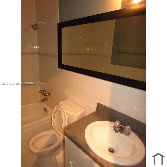 2839 Taylor Street, #3, Hollywood, Hollywood, FL 33020 Bathroom featuring a white vanity with a neutral countertop, an integrated sink, a large framed wall mirror, and a tile-surround bathtub with wall-mounted hardware