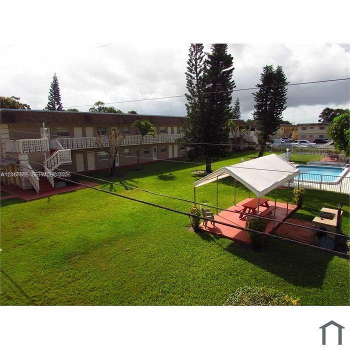 2839 Taylor Street, #3, Hollywood, Hollywood, FL 33020 Expansive common area featuring a manicured lawn, mature trees, a swimming pool with perimeter fencing, and a paved patio with a built-in barbecue station