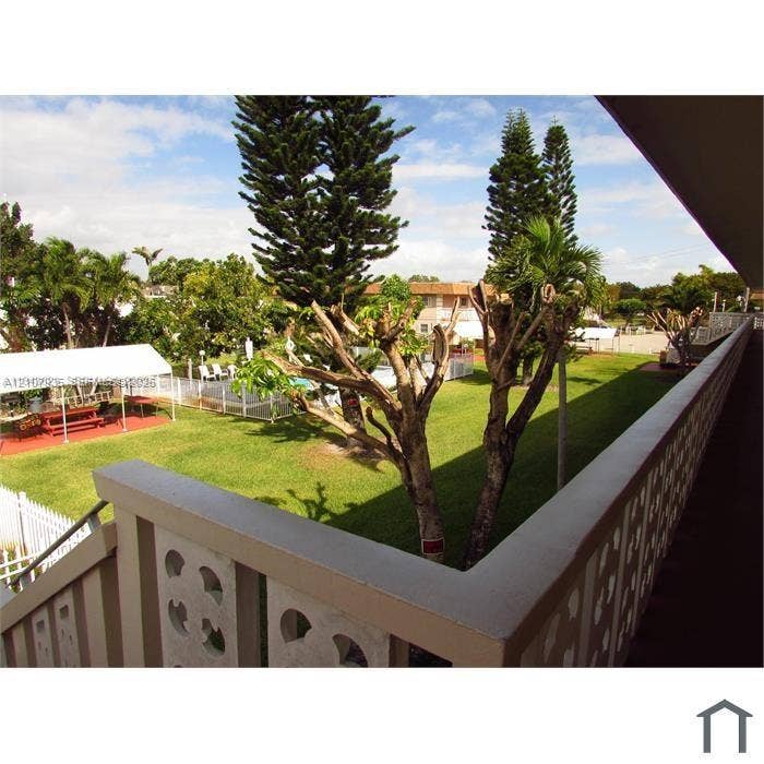 2839 Taylor Street, #3, Hollywood, Hollywood, FL 33020 Elevated exterior balcony featuring decorative breeze block railing overlooking a shared greenspace, mature landscaping, and an enclosed outdoor swimming area