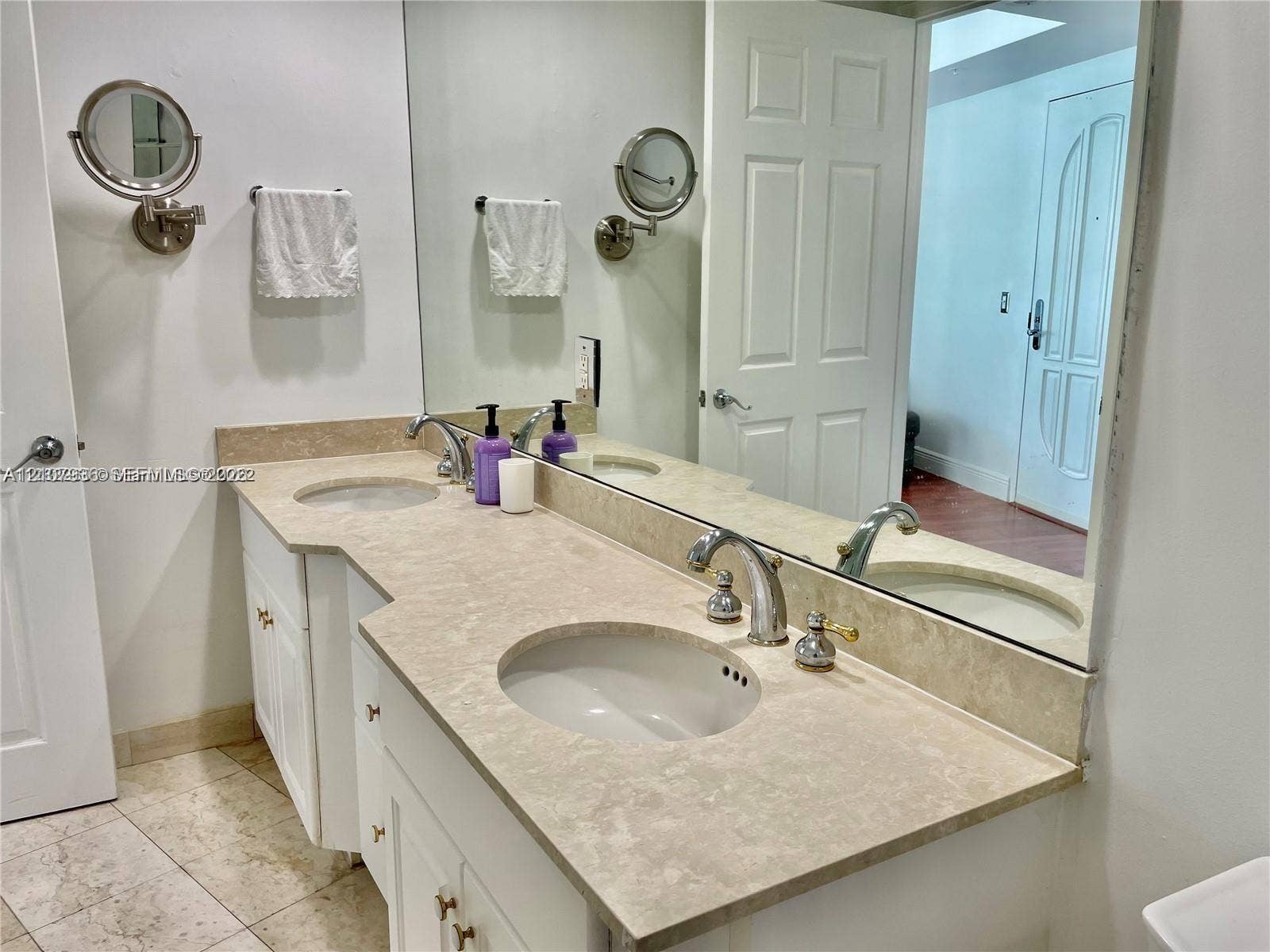 3370 Hidden Bay Drive, #510, Aventura, FL 33180 Dual-sink vanity featuring a light-toned solid surface countertop, two undermount basins, chrome-finish widespread faucets, and wall-mounted extendable mirrors