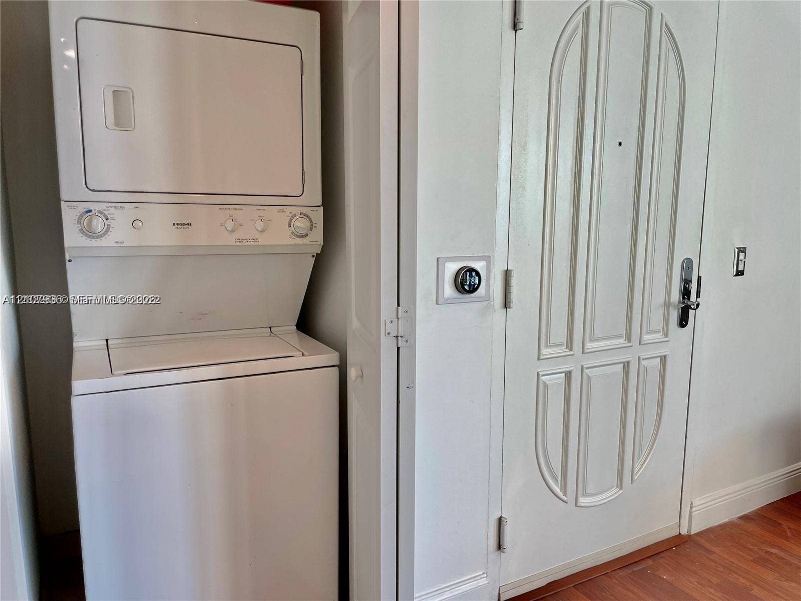 3370 Hidden Bay Drive, #510, Aventura, FL 33180 Stacked white laundry unit, wall-mounted smart thermostat, and six-panel interior door with brushed metal hardware set against wood-finish flooring