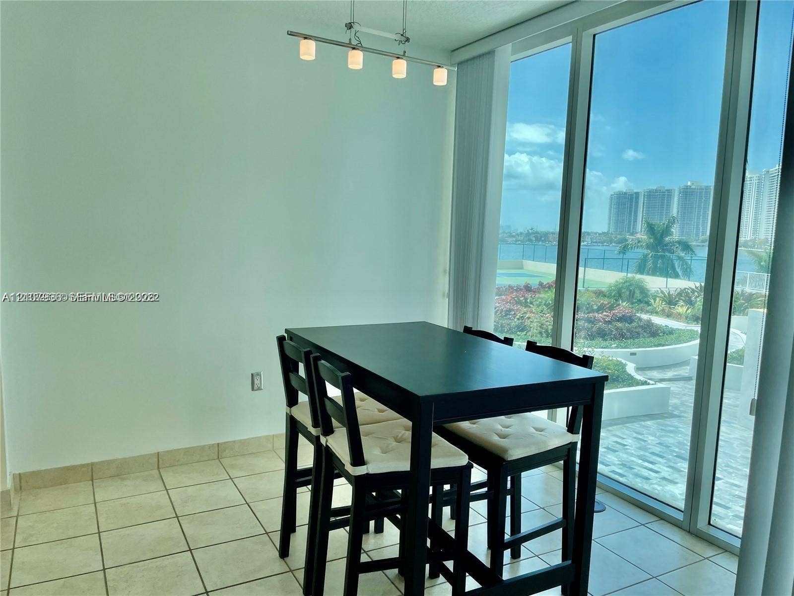 3370 Hidden Bay Drive, #510, Aventura, FL 33180 Floor-to-ceiling windows, tile flooring, four-light brushed metal track lighting, and exterior water backdrop