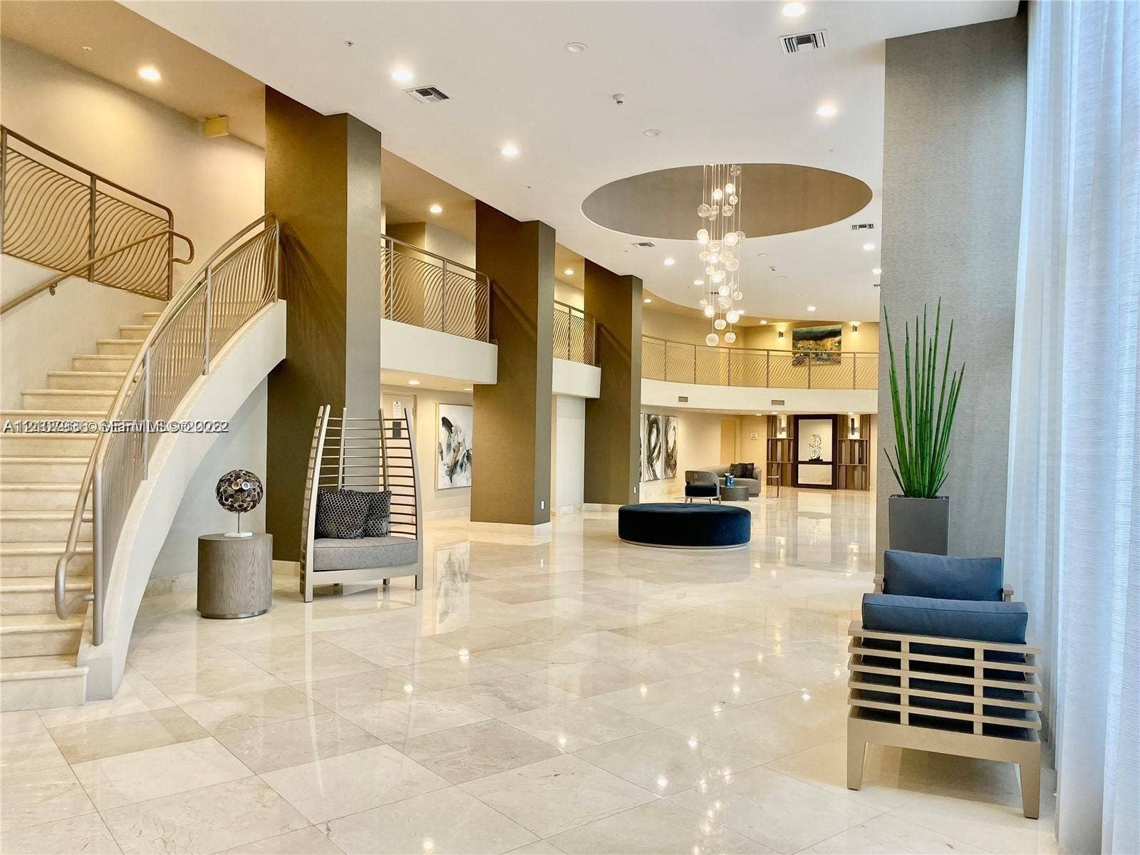 3370 Hidden Bay Drive, #510, Aventura, FL 33180 Grand lobby featuring polished stone flooring, a sweeping staircase with custom metal railing, multi-level mezzanine, and a recessed ceiling with a contemporary pendant chandelier