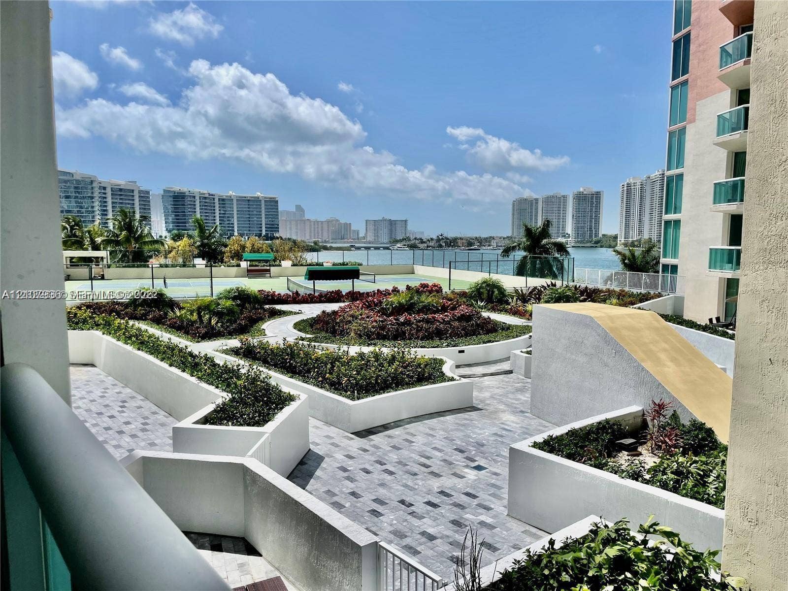 3370 Hidden Bay Drive, #510, Aventura, FL 33180 Terrace featuring paver flooring, multi-level concrete planters, and a recreational court, set against a waterfront and cityscape backdrop