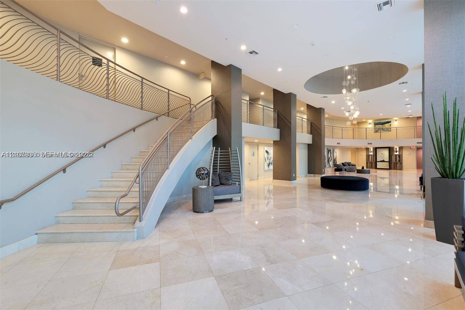 3370 Hidden Bay Drive, #510, Aventura, FL 33180 Grand lobby featuring polished stone flooring, a sweeping staircase with custom metal railings, soaring ceilings with recessed lighting, and a multi-tiered crystal chandelier