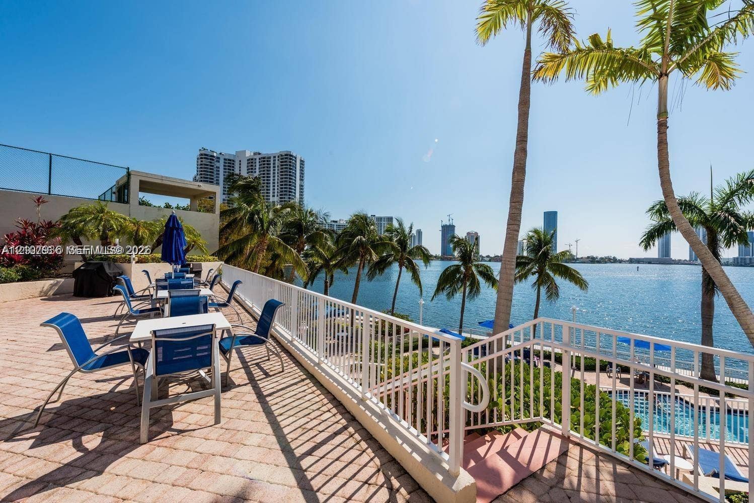 3370 Hidden Bay Drive, #510, Aventura, FL 33180 Paver-tiled terrace featuring a white metal railing, mature palm trees, and an open-air stairwell leading to a pool area