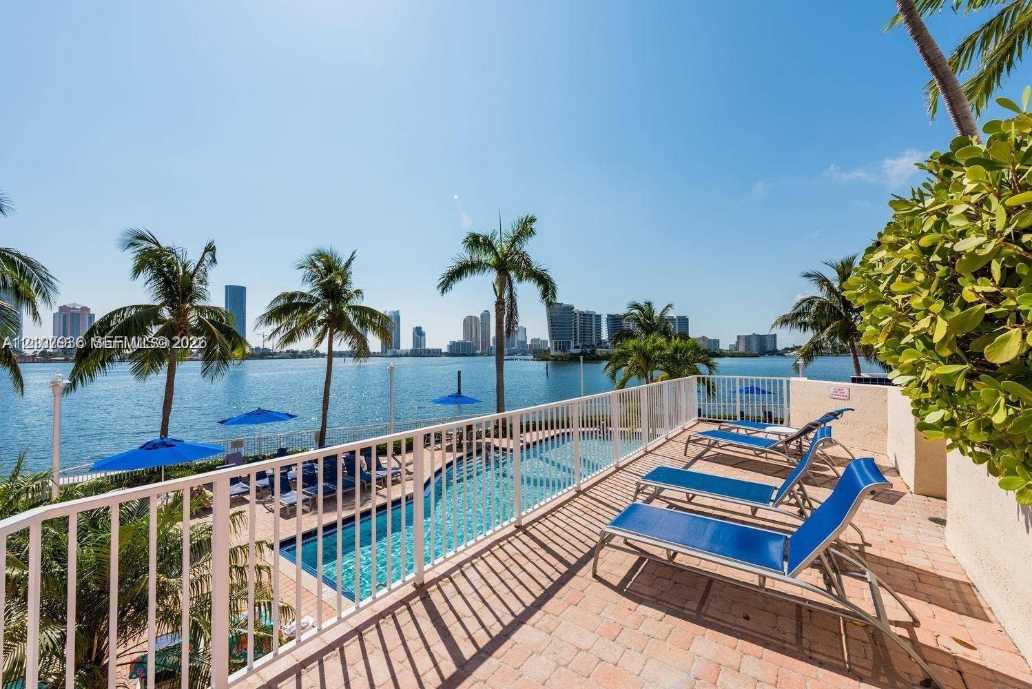 3370 Hidden Bay Drive, #510, Aventura, FL 33180 Waterfront terrace featuring a paver deck, white metal railing, and an in-ground swimming pool overlooking the bay