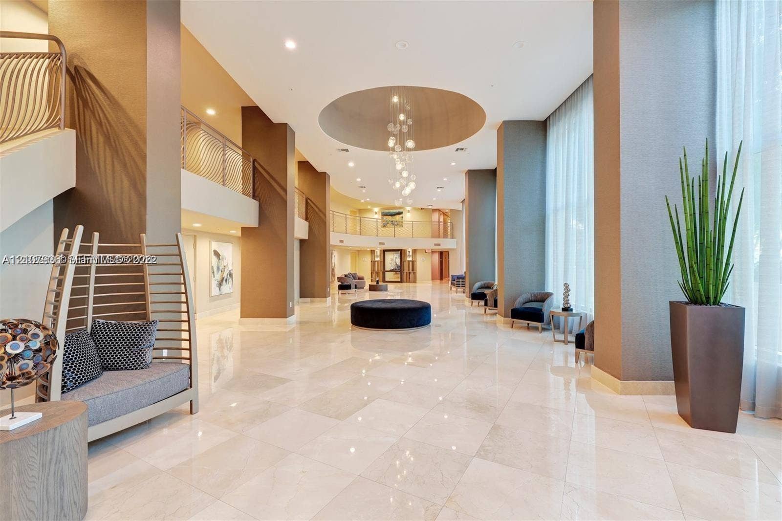 3370 Hidden Bay Drive, #510, Aventura, FL 33180 Grand lobby featuring high ceilings, polished stone flooring, a multi-tiered circular ceiling medallion with recessed lighting, suspended light fixtures, and a structural mezzanine level with metal railings