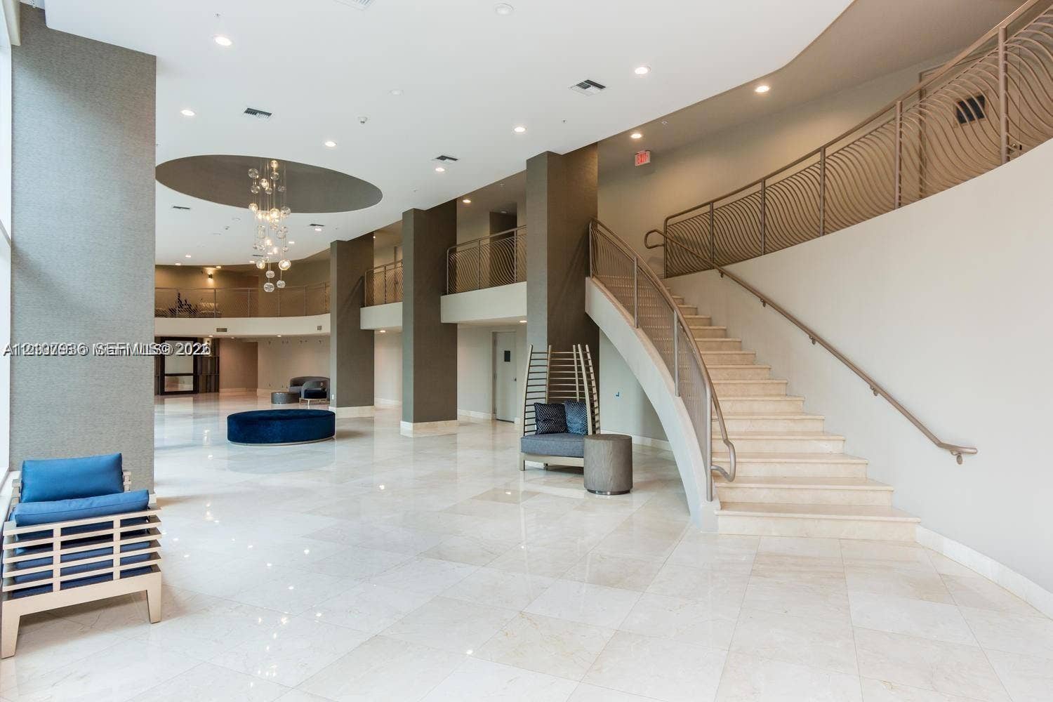 3370 Hidden Bay Drive, #510, Aventura, FL 33180 Expansive multi-level lobby featuring polished stone flooring, a curved staircase with metal railings, recessed ceiling lighting, and a decorative circular ceiling inlay with integrated light fixture