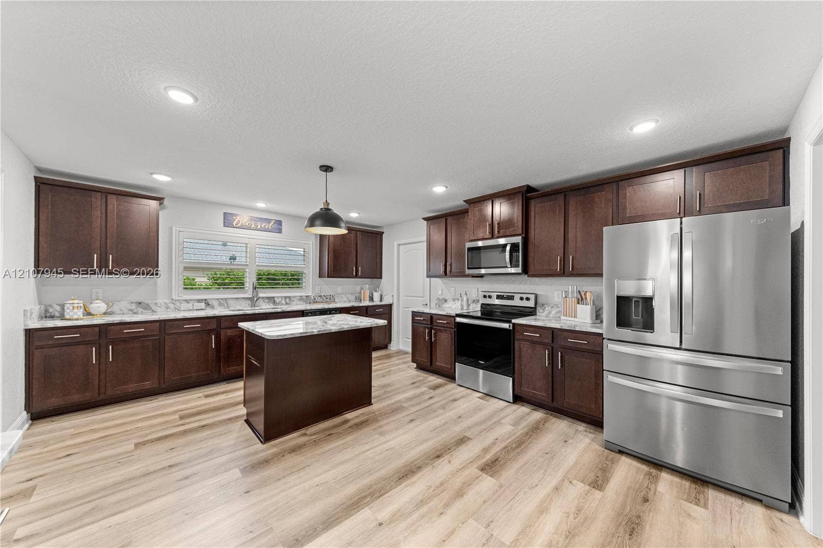 Kitchen featuring dark wood cabinetry, stone-surface countertops, central island, stainless steel appliances, and wood-finish flooring