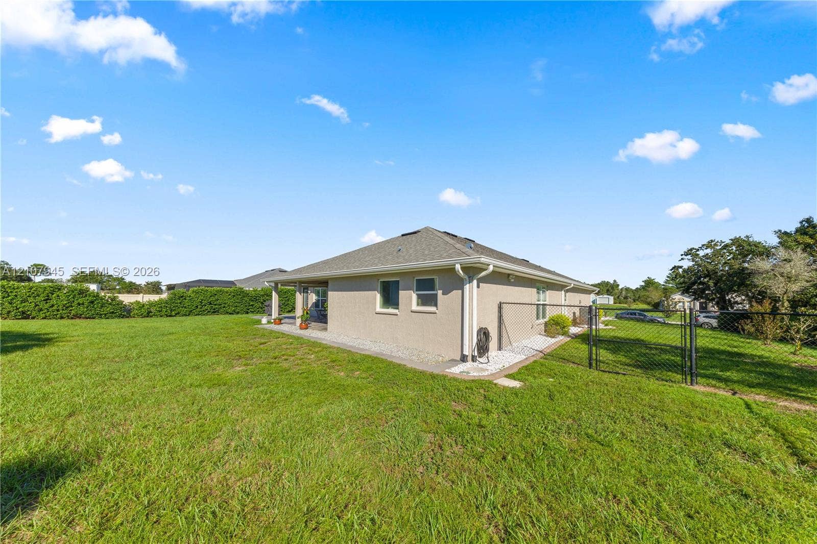 Expansive backyard featuring a sprawling grass lawn, perimeter chain-link fencing, concrete patio, and stone gravel foundation border