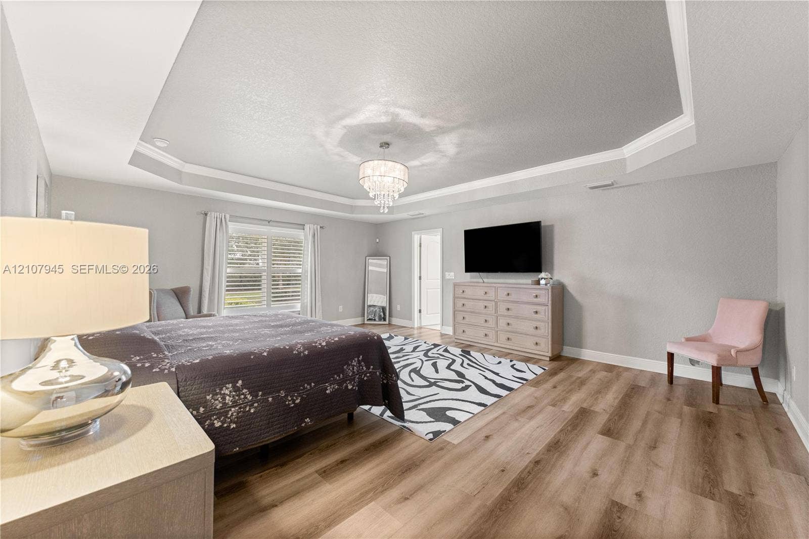 Tray ceiling with crown molding, wood-finish flooring, and a crystal chandelier