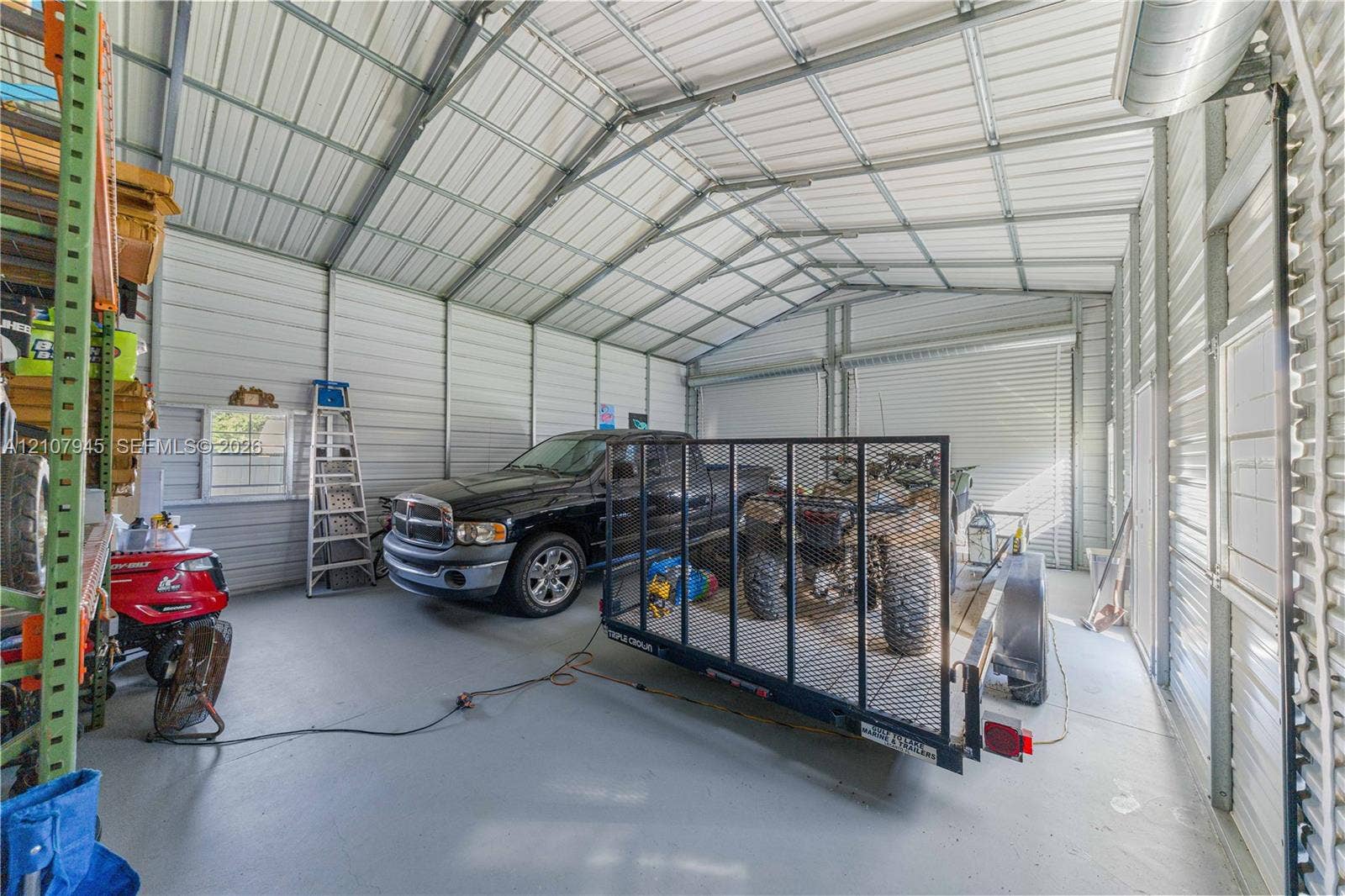 Detached metal structure featuring a vaulted ceiling, finished concrete flooring, exposed steel framing, and a roll-up vehicle door