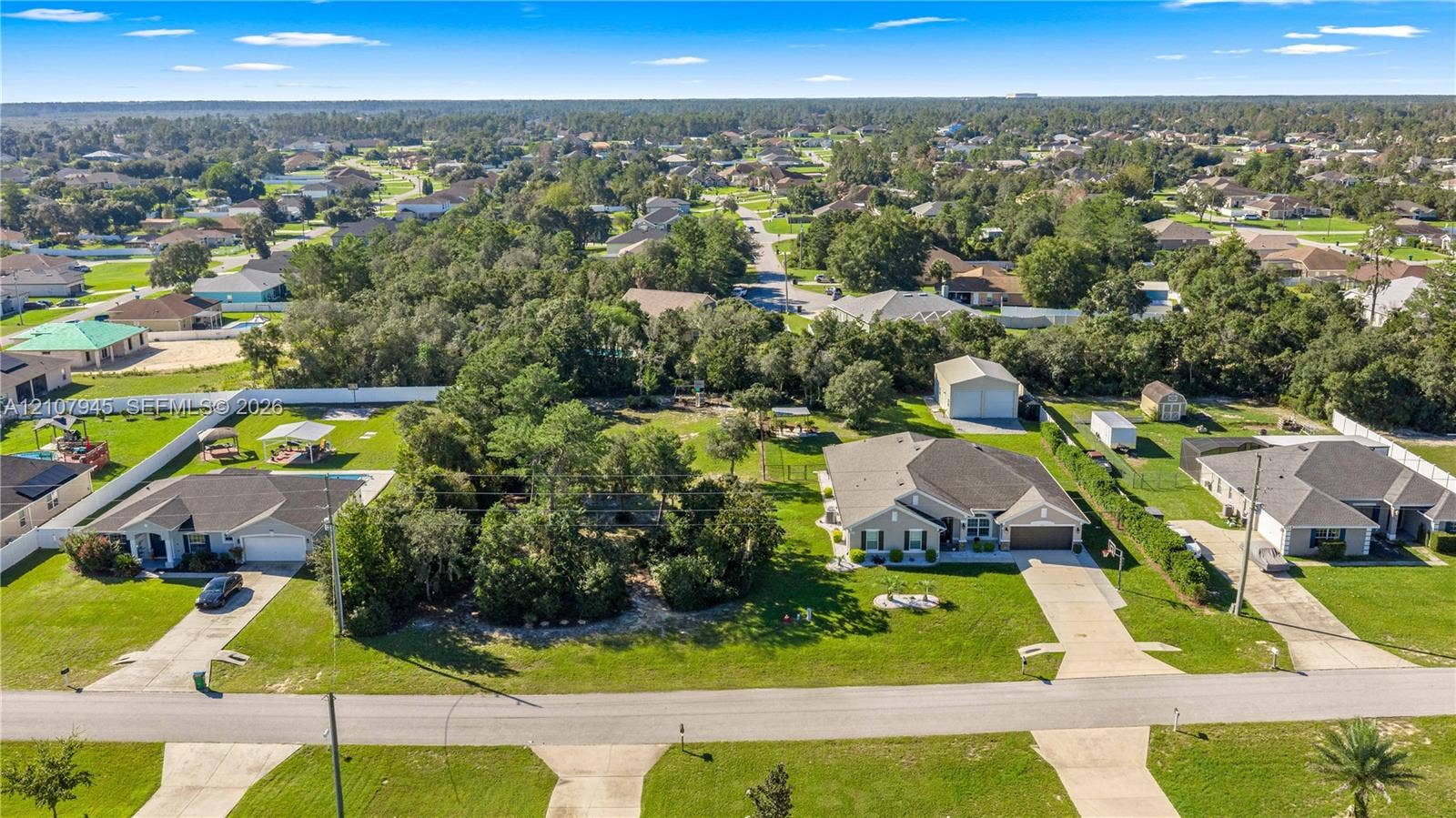 Aerial perspective of a residential property featuring a sprawling corner lot, a detached garage, a fenced rear perimeter, and mature tree landscaping