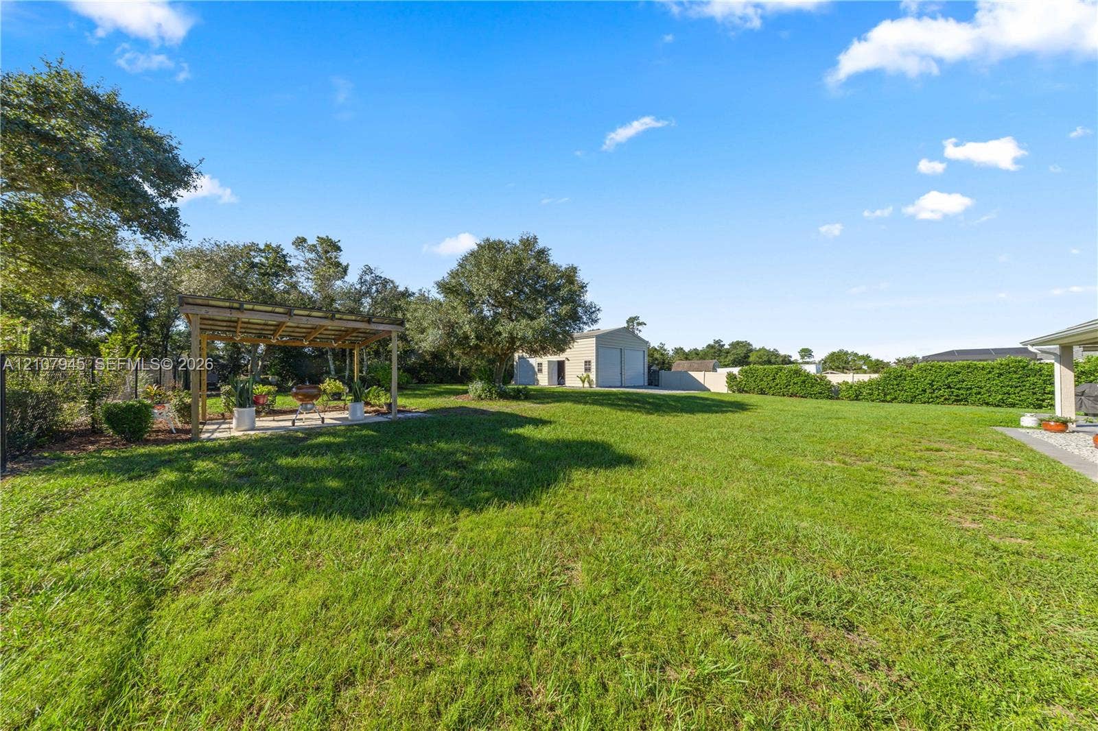 Expansive backyard featuring a large grass lawn, a wood-framed pergola, and a detached two-car garage