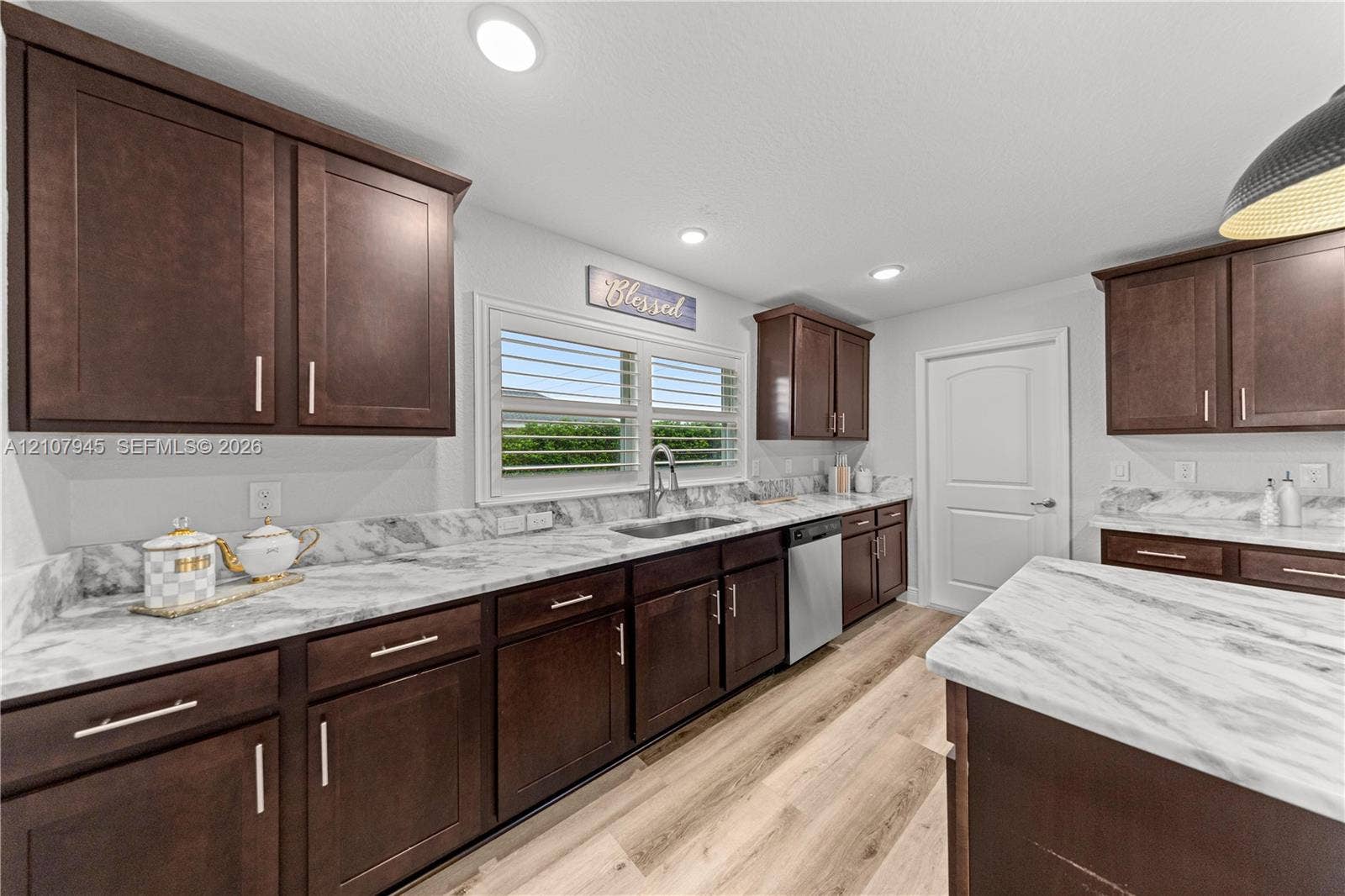 Kitchen featuring dark-finish cabinetry, stone-pattern countertops, stainless steel sink with pull-down faucet, wood-finish flooring, and recessed ceiling lighting