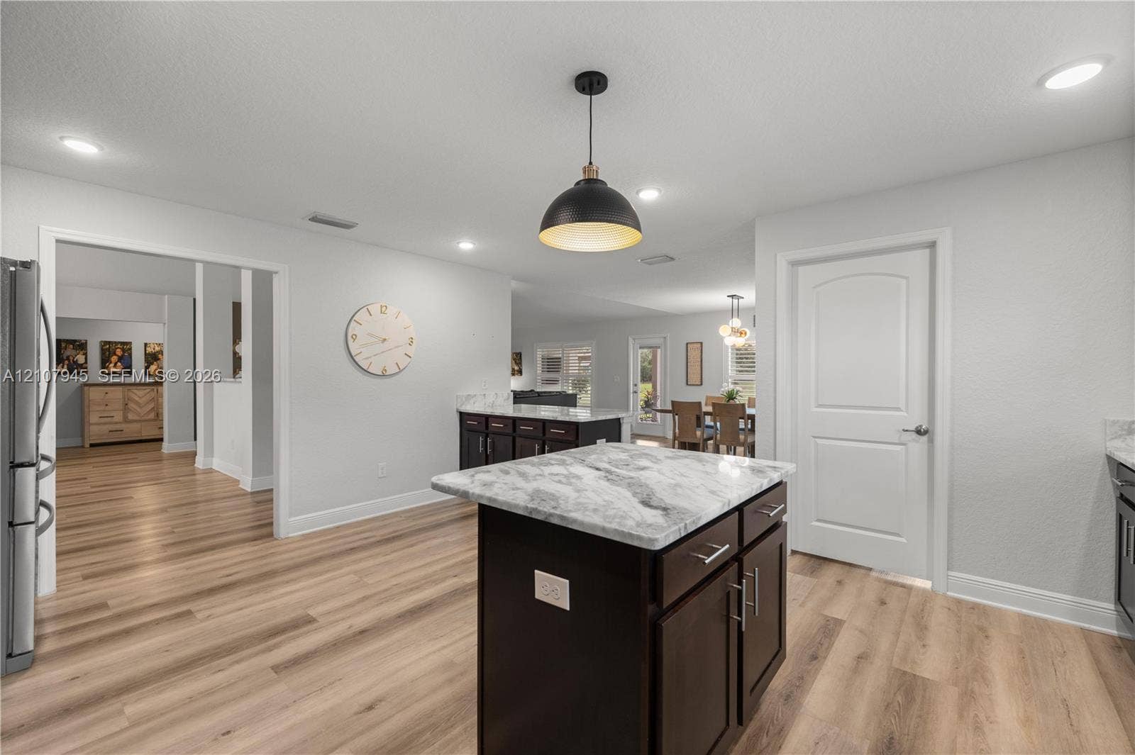 Kitchen featuring a central island with stone-finish countertops, wood-finish flooring, dark-toned cabinetry, and recessed lighting