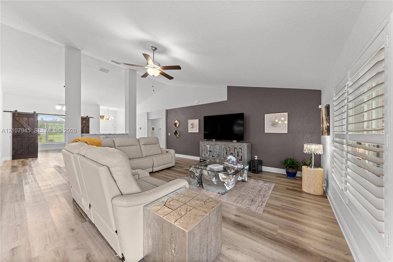 Vaulted ceilings, wood-finish flooring, accent wall, ceiling fan, and plantation shutters