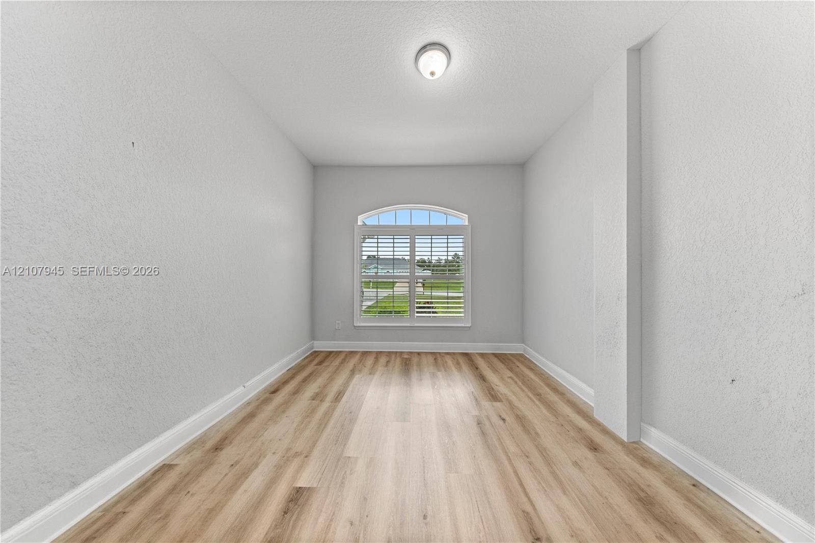 Interior room featuring wood-finish flooring, an arched window with plantation shutters, and a flush-mount ceiling fixture