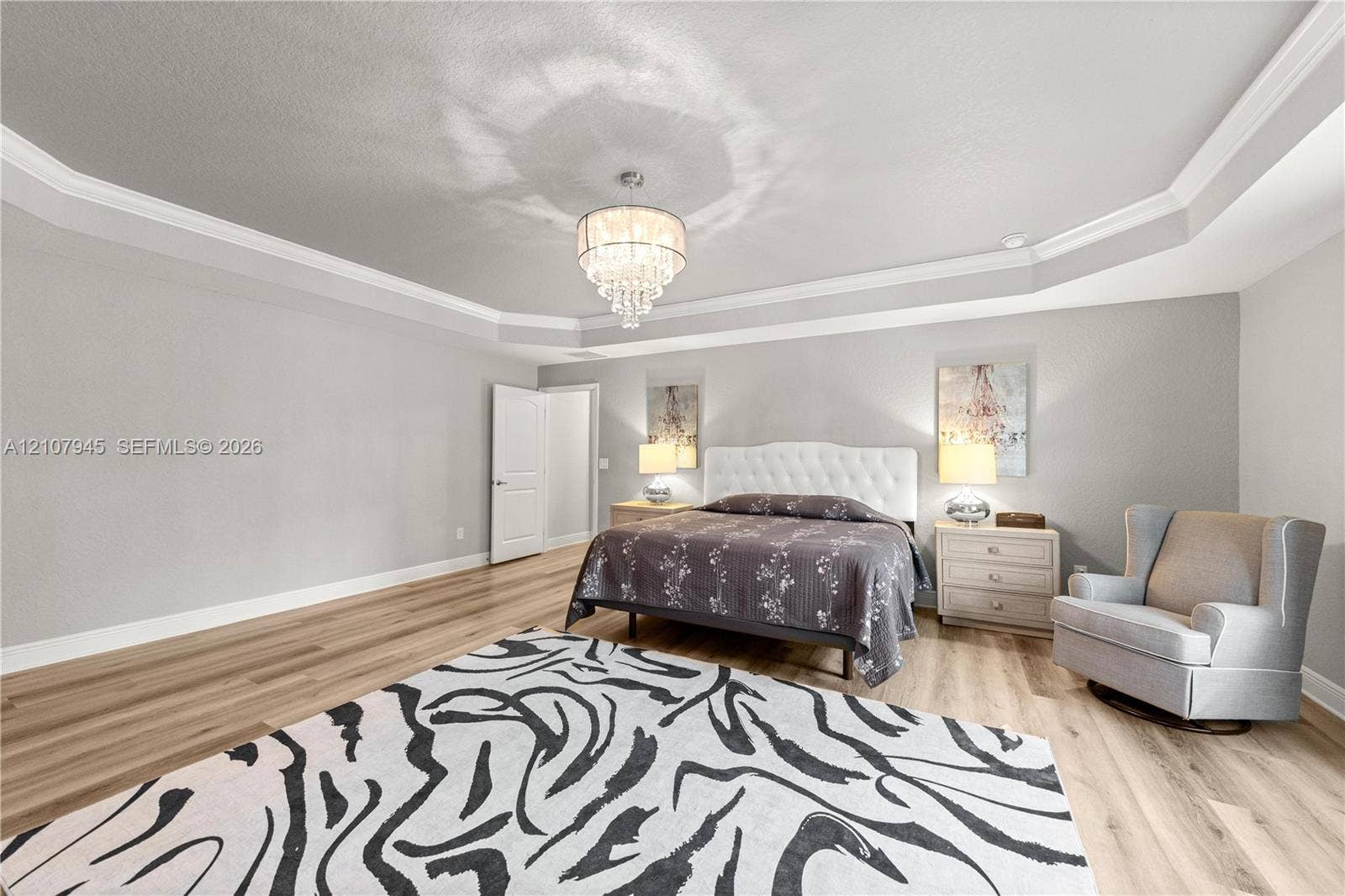 Tray ceiling featuring multi-tiered crown molding, wood-finish flooring, and a crystal chandelier